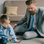 7 Dicas para Equilibrar Vida Pessoal e Profissional - empresário de terno e filho pequeno brincando com carros de brinquedo no chão em casa, equilíbrio entre trabalho e vida